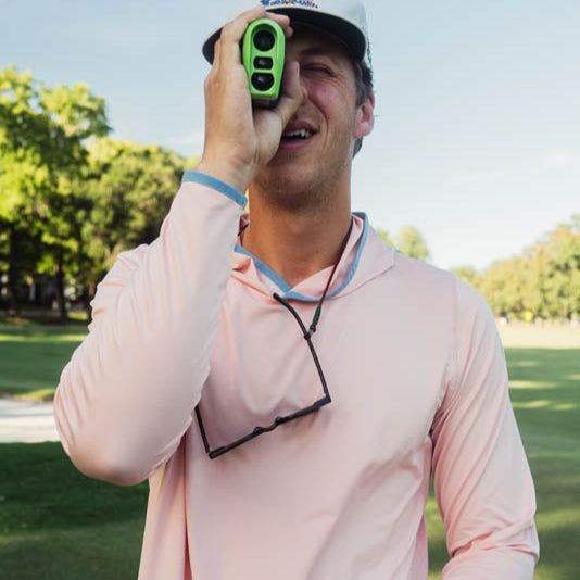Man in pink long-sleeve shirt holding a smartphone with a golf club on a golf course