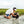 Person kneeling on a sandy beach with a dog, surrounded by grass and water.