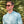 Man wearing sunglasses and a light blue shirt in front of green foliage